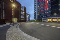 the empty street is lined with red brick and grey buildings at dusk, in a wide, quiet city area