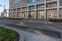 an empty street near a large building in front of it with cars parked on the road