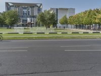 a street with grass, trees and a building behind it is one empty road with no traffic in front