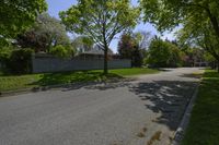 a empty street lined with homes and trees in a neighborhood setting with grassy lawn area,