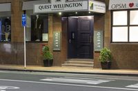 a photo of a sign for the quiet wellington hotel on a street corner with plants