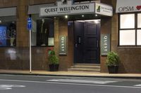 a photo of a sign for the quiet wellington hotel on a street corner with plants