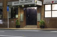 a photo of a sign for the quiet wellington hotel on a street corner with plants