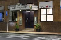 a photo of a sign for the quiet wellington hotel on a street corner with plants