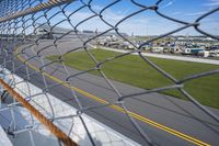 race cars race up an empty track as seen from behind a chain - link fence