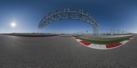 the image shows an asphalted race track with a bridge over it and blue sky in the background