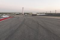 an asphalt racing track with cars passing by it, at dusk with sky light in distance