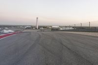 an asphalt racing track with cars passing by it, at dusk with sky light in distance