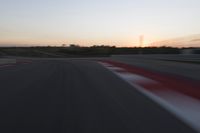 Race Track at Dawn: An Automobile Speeds Along the Line