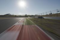 a view of the sun from a vehicle in motion on a race track in a blurry, light filled, open area