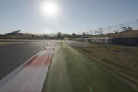 a view of the sun from a vehicle in motion on a race track in a blurry, light filled, open area