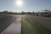 a view of the sun from a vehicle in motion on a race track in a blurry, light filled, open area