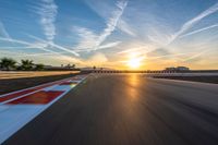 a photo of a dirt race track with sun setting in the distance of the track