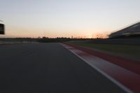 blurred speed - moving image of a race track at sunset with red and white stripes