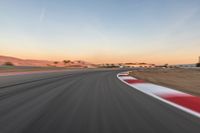 a photo of a dirt race track with sun setting in the distance of the track