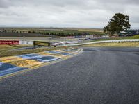 a race track with the track covered in patches of yellow paint and signs, as well as a truck, with some cars in the road