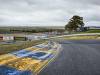 a race track with the track covered in patches of yellow paint and signs, as well as a truck, with some cars in the road