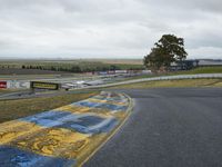 a race track with the track covered in patches of yellow paint and signs, as well as a truck, with some cars in the road