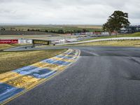 a race track with the track covered in patches of yellow paint and signs, as well as a truck, with some cars in the road