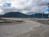 a railroad crossing in the middle of the wilderness over the water, with snow on the mountains beyond