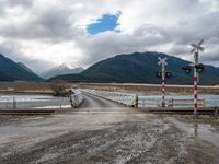 a railroad crossing in the middle of the wilderness over the water, with snow on the mountains beyond