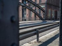 railroad tracks at the station with a metal bridge in the background as seen through a metal gate