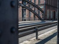 railroad tracks at the station with a metal bridge in the background as seen through a metal gate