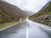 empty road near grassy hillsides and mountains with fog in background at daytime time, with mountain range visible