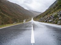 empty road near grassy hillsides and mountains with fog in background at daytime time, with mountain range visible