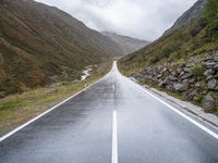 empty road near grassy hillsides and mountains with fog in background at daytime time, with mountain range visible