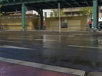 a woman walking down a rain soaked road with an umbrella in the foreground and overpass