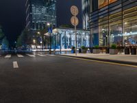 a night time view of a bus stop and street with illuminated buildings in the background