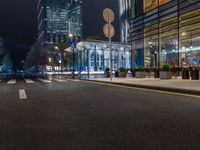 a night time view of a bus stop and street with illuminated buildings in the background