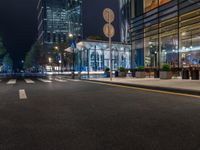 a night time view of a bus stop and street with illuminated buildings in the background