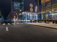 a night time view of a bus stop and street with illuminated buildings in the background