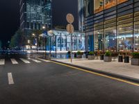 a night time view of a bus stop and street with illuminated buildings in the background