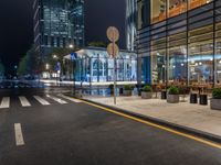 a night time view of a bus stop and street with illuminated buildings in the background