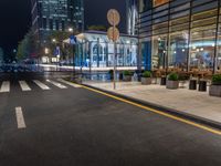 a night time view of a bus stop and street with illuminated buildings in the background