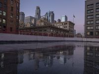 city buildings reflecting in the water on a rainy day with purple skies above them and city streets reflected in wet puddles of water