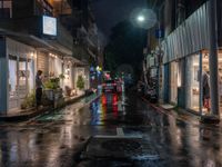 a wet city street filled with cars sitting under a moon lit sky on a rainy night