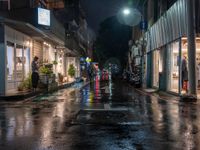 a wet city street filled with cars sitting under a moon lit sky on a rainy night