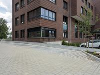 brick sidewalk on side of building with large windows and plants outside, and sidewalk blocker along street