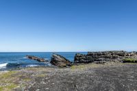 some rocks and water on the shore line the beach under a blue sky with some green grass