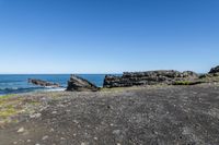 some rocks and water on the shore line the beach under a blue sky with some green grass