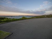 a person rides their skate board near the water and a city in the distance at dusk