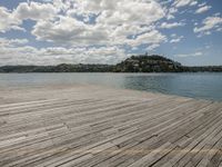 a dock sits near the ocean, in front of some clouds and hills in the distance