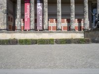 an outdoor stone walk in front of two columns in the building with flags and statues