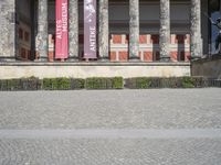 an outdoor stone walk in front of two columns in the building with flags and statues