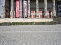 an outdoor stone walk in front of two columns in the building with flags and statues