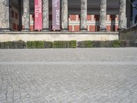 an outdoor stone walk in front of two columns in the building with flags and statues